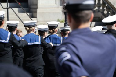 Arkadan yakından bakınca, koyu mavi üniformalı, düz şapkalı, lacivert üniformalı birçok kişi görülüyor. Görünür yüzleri veya özel işaretleri olmayan başları ve omuzlarına verilen ilgi, birlik ve disiplini vurguluyor..