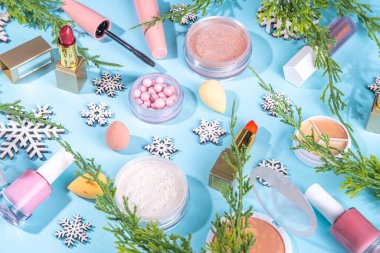 Yapay kar taneleri ve Noel ağacı dallarıyla açık mavi arkaplanda kış makyajı yapılıyor. Çeşitli makyaj malzemeleri, gölgeler, ruj, rimel, allık. Noel güzellik indirimi