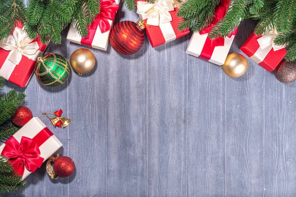プレゼントボックス木製の背景にクリスマスツリー付き お祝いのリボン モミの木の枝と古いグレーの板の上にクリスマスの装飾を持つ様々な赤と白の贈り物トップビューのコピースペース — ストック写真