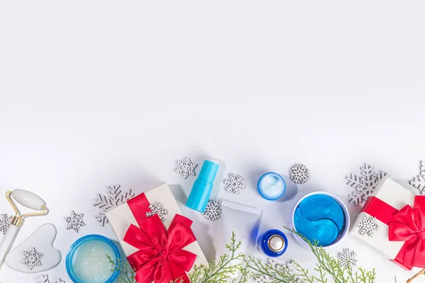 Winter skin care and hand care cosmetic in unbranded containers, bottles, tubes with artificial snowflakes, Christmas tree branches and gift boxes. Christmas New Year winter cosmetics sale flat lay