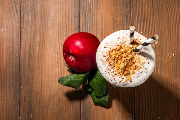 Homemade loaded apple pie milk shake, red autumn apple protein smoothie with tart crumble and spices, healthy fall seasonal breakfast drink, on cozy wooden background copy space