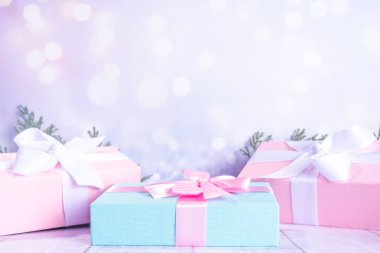 Pastel Noel arkaplanı mavi ve pembe hediyelerle donatılmış, çam ağacı dalları hafif karlı şenlik ışıkları bulanık arka plan fotokopi alanı