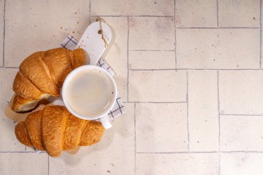 Taze pişmiş kruvasan ve bej kaplamalı kahve fincanı. Arka planda fotokopi alanı.