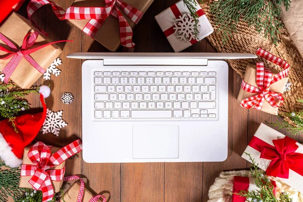 Laptop computer with Christmas gift boxes from above on wooden background. Notebook with presents, fir tree and winter decor. Preparation for Christmas, New Year