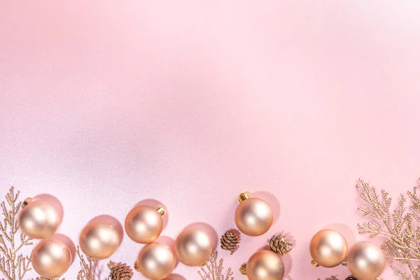 Rose gold Christmas, New Year background with golden christmas tree twigs and balls, holiday gift boxes, decorations, artifical snow, flat lay on pink background copy space
