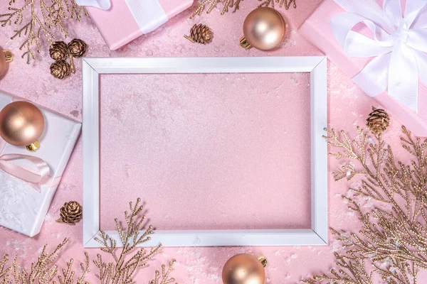 Rose gold Christmas, New Year background with golden christmas tree twigs and balls, holiday gift boxes, decorations, artifical snow, flat lay on pink background copy space