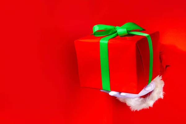 圣诞快乐贺卡明亮的红色背景 礼品和促销横幅背景 圣诞老人手拿着大大的红色礼品盒 上面有红色撕破的纸孔背景 上面有喜庆的绿带 — 图库照片