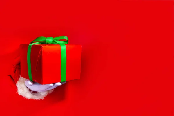 圣诞快乐贺卡明亮的红色背景 礼品和促销横幅背景 圣诞老人手拿着大大的红色礼品盒 上面有红色撕破的纸孔背景 上面有喜庆的绿带 — 图库照片