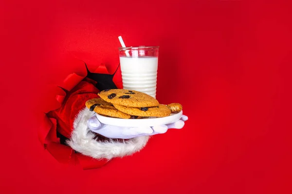 伝統的なクリスマスクッキーのスナックとサンタクロースの手ミルクグラス Santa Dunking Cookieは 明るいお祝いの赤い破れた紙の穴の背景にあります メリークリスマスとハッピーニューイヤーグリーティングカード — ストック写真