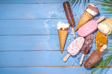 Siyah arka planda çeşitli dondurma setleri. Tahta mavi plaj zemininde buzlu dondurma ve koni çeşitleri ve tropikal palmiye yaprakları üst düz görünüm kopya alanı