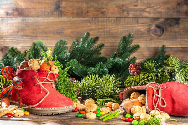 Sinterklaas, Saint Nicholas day background. Little kid red shoe with carrots and sweets, trooigoed, pepernoten, candy. Dutch Christmas holiday on cozy wooden background. 