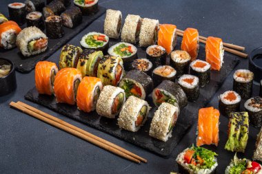 Suşi, soya sosu, zencefil ve yemek çubuklarıyla birlikte koyu arkaplan üzerine kuruludur.