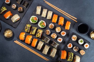 Suşi, soya sosu, zencefil ve yemek çubuklarıyla birlikte koyu arkaplan üzerine kuruludur.