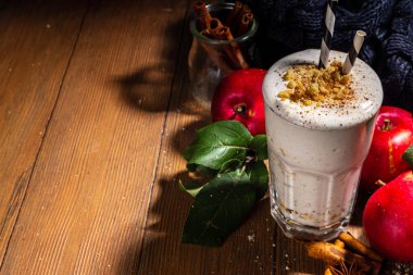 Ev yapımı elmalı turta milkshake, tart parçacıkları ve baharatlı kırmızı sonbahar elma proteini smoothie, sıcacık ahşap arka planda mevsimlik sağlıklı bir kahvaltı içeceği.