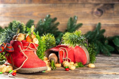 Sinterklaas, Saint Nicholas day background. Little kid red shoe with carrots and sweets, trooigoed, pepernoten, candy. Dutch Christmas holiday on cozy wooden background. 