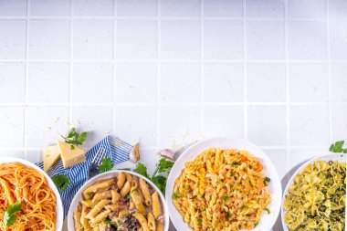Beyaz fayanslı arka planda farklı soslu makarna seti. Spagetti, farfalle, makarna, deniz ürünleri, ıspanak, karbonara, domates soslu fusilli makarna. İtalyan yemeği, Akdeniz yemeği konsepti