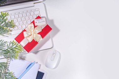 İş yerindeki gizli Noel Baba 'dan hediye. Ofis Noel ve Yeni Yıl kutlama oyunu. Ofis masası yüzeyi, neşeli hediye kutusu olan defter, beyaz arkaplan düz kopya alanı