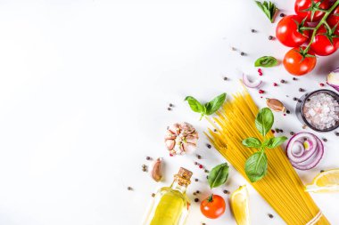Makarna pişirmek için İtalyan yemekleri. Çeşitli malzemeli çiğ spagetti makarna - soğan, domates, sarımsak, fesleğen, maydanoz, peynir, zeytinyağı. Beyaz tablo arkaplanında, düz kopya alanı