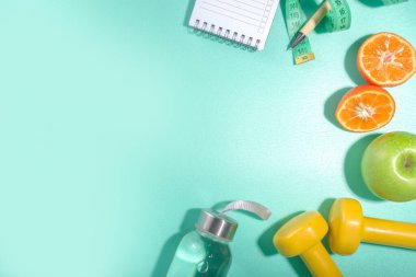 Bahar, yaz zayıflama mevsimi konsepti. Sulu spor şişesi, fitness dambılları, plaj şezlongu dekor, mezura, not defteri, elma, açık mavi arka planda dilimlenmiş turuncu. Düz kopya alanı üst görünümü
