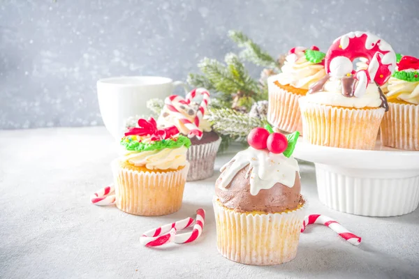 Funny Christmas cupcakes. Homemade sweet cupcakes with sugar glaze in form on christmas decoration and symbols, on wooden background with xmas decor
