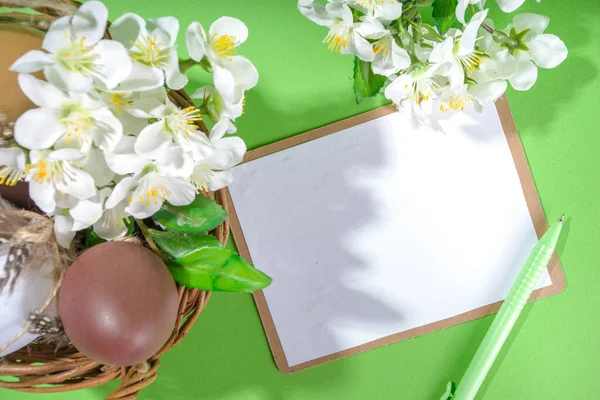 Happy Easter greeting card background, mockup with Easter eggs, spring cherry blooming flowers in small basket, wooden and green background copy space