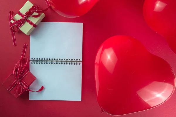Valentine day sweet holiday background with red heart shaped balloons on red background, with notepad, tablet, flatlay top view frame copy space, mock up for Valentine greeting card