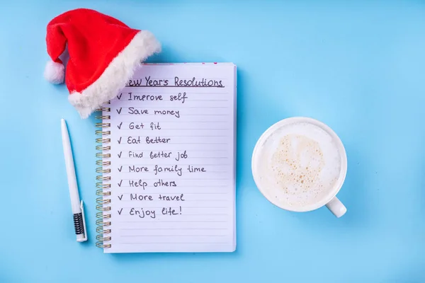New Year plan goals List on notebook with Santa hat, coffee latte or hot chocolate cup, simple New Year goals List 2023, plan listing of new year beginnings goals flat lay background, banner