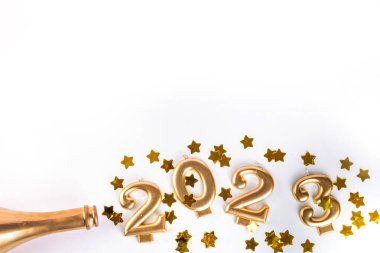 Yeni yıl 2023. Altın şampanya şişesi, konfeti yıldızları, beyaz arka planda 2023 numara.