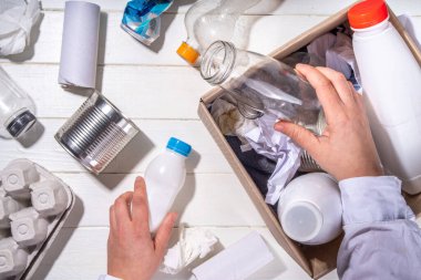 Çöp ayıklama, atık geri dönüşüm konsepti. Geri dönüşüm malzemelerinin olduğu kutu - plastik, cam, kağıt, karton, beyaz ahşap arka plan fotokopi alanı. Kadın elleri çeşitli çöp ve çöpleri ayırıyor.