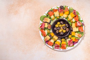 Noel partisi yemeği, modaya uygun mezeler. Sosis, et, peynir, zeytin, bej masa arkaplanındaki yeşillikler ve altın rengi Noel dekorasyonundan yapılmış çelenk.