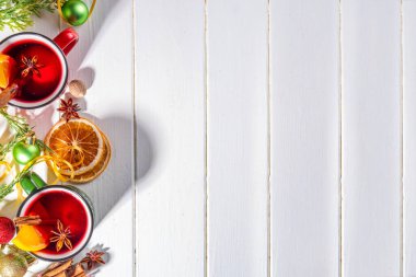 Noel kışında sıcak şarap içilir. Klasik tarz, turuncu dilimli, tarçınlı, baharatlı kırmızı şarap kokteyli Noel bayramında, dekore edilmiş beyaz ahşap arka plan fotokopi alanı.