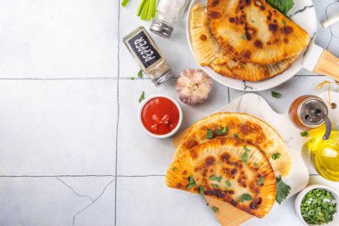 Cheburekler, börekler. Kızarmış turtalar, et ve baharatlı, otlar ve domates sosuyla beyaz fayanslı arka planda.