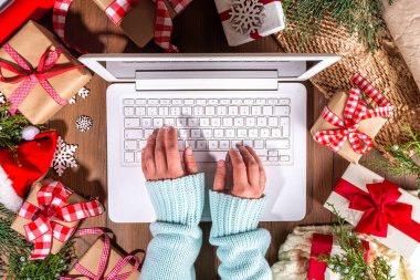 Tahta arka planda Noel hediyesi kutuları olan dizüstü bilgisayar kullanan biri. Kadın eli hediyeli defter, köknar ağacı ve kış dekoru. Noel ve Yeni Yıl için Hazırlık