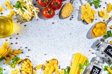 Beyaz masa arkasında çeşitli kurutulmuş spagetti, makarna ve kaşıklarla hazırlanmış makarna. Farklı şekillerde çiğ İtalyan makarnası, otlar, zeytinyağı, domatesler, baharatlar.