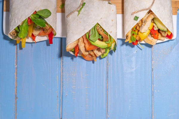 Klasik sokak yemeği shawarma ya da burrito, kızarmış tavuk eti, taze sebze, sos, parlak mavi ahşap arka plan, düz görünüm fotokopi alanı ile kaplanmış sağlıklı sandviç.