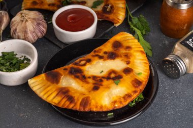 Cheburekler, börekler. Kızarmış turtalar, et ve baharatlı, otlar ve domates sosuyla birlikte siyah beton bir arka planda.