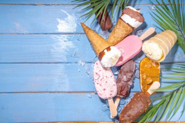 Siyah arka planda çeşitli dondurma setleri. Tahta mavi plaj zemininde buzlu dondurma ve koni çeşitleri ve tropikal palmiye yaprakları üst düz görünüm kopya alanı