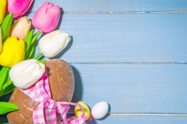 Paskalya bayramı tebrik kartı arka planı, çikolatalı tavşan, yumurta ve lale çiçekleri, açık mavi arka plan düz çerçeve çerçeve fotokopi alanı üst görünümü üzerinde