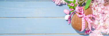 Paskalya bayramı tebrik kartı arka planı, çikolata yumurtaları ve çiçek açan bahar çiçekleri, açık mavi arka plan düz çerçeve fotokopi alanı üst görünümü