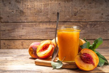 Red peach jam in small jar. Homemade autumn peach jam with fresh fruits. Fall preparations and canning on wooden table background copy space