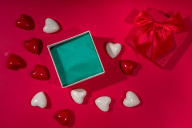 Sevgililer Günü tatili geçmişi. Kurdeleli el işi kağıt hediye kutusu, gül çiçekleri ve kalpler dekorasyonu, kırmızı arkaplan üst görünümü üzerinde kopyalama alanı