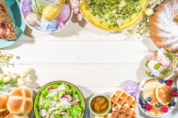 Festive dinner, Easter brunch. Traditional Easter dishes on family home table - baked meat, quiche, spring salad, muffin, colored eggs, hot cross buns