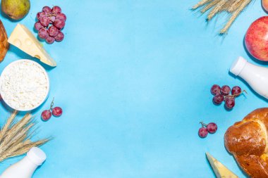 Yahudi bayramının sembolleri olan mutlu Shavuot tebrik kartı - nar, üzüm, elma, tatlı challah ekmeği, buğday filizi, süt, peynir, süzme peynir, açık mavi zemin