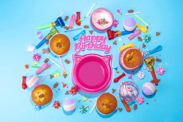 Pet happy birthday background with set different cats and kitty snack, food and toys, cat muzzle shape bowl, birthday cupcakes with happy birthday candles, accessories. Flatlay on blue background top view