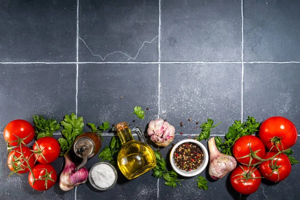 Cooking ingredients background. Spices, black pepper, garlic, onion, greens, tomatoes. olive oil on black tiled  table top view copy space. Preparation healthy food background.