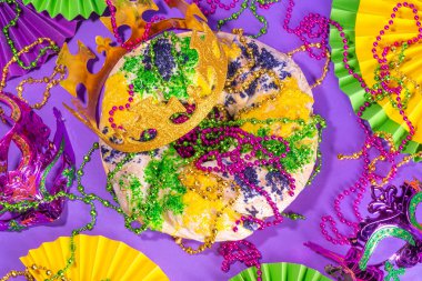 King Cake for Mardi Gras, traditional New Orlean Mardi Gras holiday pastry with plastic baby, with festival masquerade accessories, decor, carnival mask, beads
