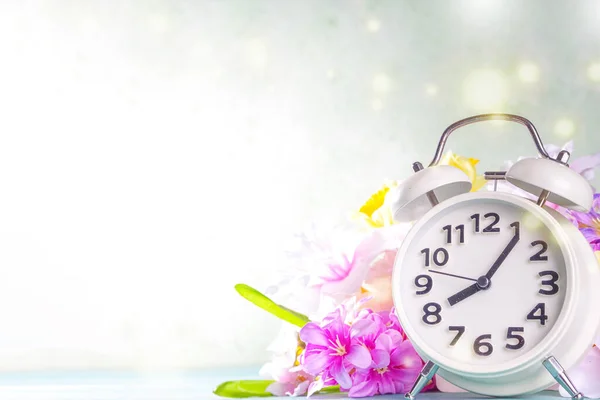Spring Time Change concept. Summer back concept. Vintage alarm Clock with fresh, beautiful spring flower on sun lighted background banner background copy space