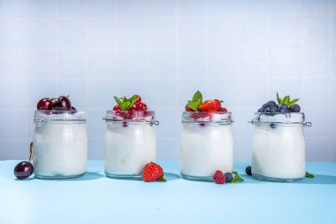 Variety of yogurt in portion glass jars. Healthy summer breakfast concept, with seasonal berry  strawberry, cherry, blueberry, currant 