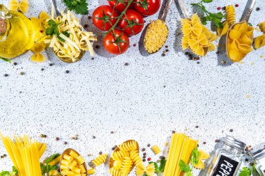 Beyaz masa arkasında çeşitli kurutulmuş spagetti, makarna ve kaşıklarla hazırlanmış makarna. Farklı şekillerde çiğ İtalyan makarnası, otlar, zeytinyağı, domatesler, baharatlar.