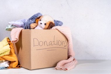 Giysileri, oyuncakları ve yiyeceği beyaz masa arkasında olan bağış kutusu. Oyuncak, kadın ve çocuk kıyafetleri ve yiyeceklerle dolu bir karton bağış kutusu. Sosyal hizmet, gönüllülük, yardım konsepti kopyalama alanı
